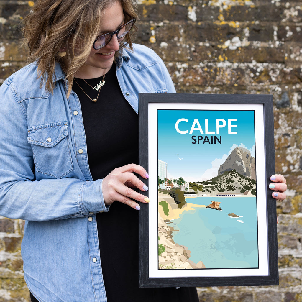 a woman holding up a framed poster in front of a brick wall